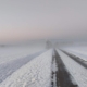 Verschneite neblige Straße mit einer Spur im Sonnenaufang