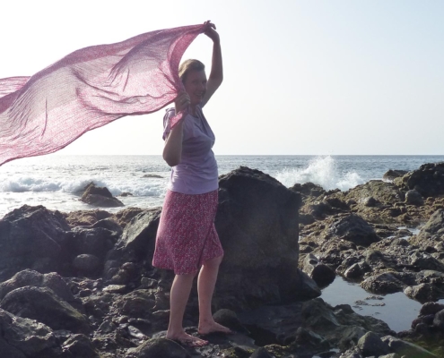 Patricia mit rotem Schal im Wind am Meer auf Klippen