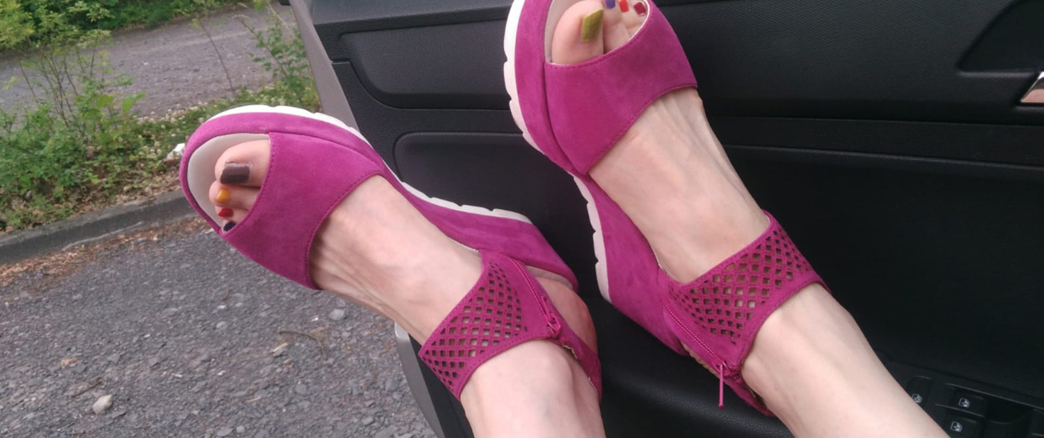 Pinkfarbene Sandalen mit bunten Fußnägeln, die auf der Autotüre liegen Pinkfarbene Sandalen mit bunten Fußnägeln, die auf der Autotüre liegen